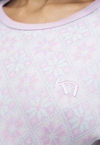 Gros plan sur un tissu violet clair avec un motif subtil de flocons de neige et une lettre stylisée brodée "K" près de l'encolure.