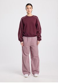 Burgundy sweatshirt with white piping and relaxed fit, paired with wide-leg red and white striped pants, textured fabric, and elastic waistband.