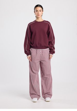 Sweat-shirt bordeaux avec passepoil blanc et coupe décontractée, associé à un pantalon à jambes larges rayé rouge et blanc, en tissu texturé, avec une taille élastique.