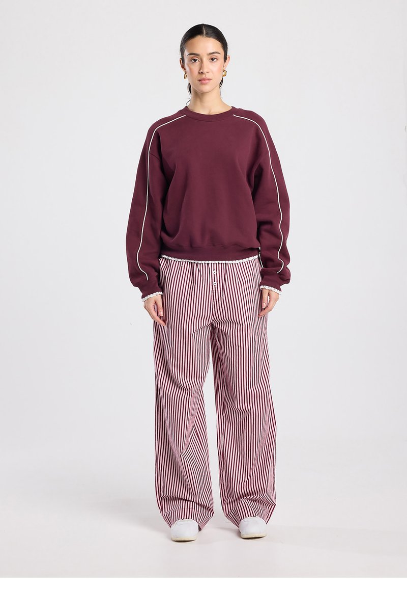 Burgundy sweatshirt with white piping and relaxed fit, paired with wide-leg red and white striped pants, textured fabric, and elastic waistband.