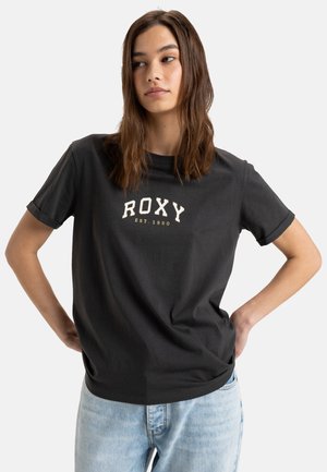 T-shirt en coton noir avec un logo "ROXY" blanc et le texte "EST. 1990". Manches courtes avec bords retroussés et coupe décontractée.
