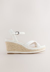 Sandale compensée blanche tressée avec bride cheville, fermeture à boucle et semelle plateforme en corde tressée.