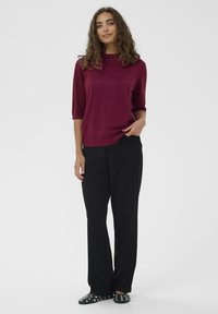 Burgundská metalická pletená blúzka s vysokým výstrihom a rukávmi po lakte, kombinovaná s voľnými čiernymi nohavicami a čiernou obuvou so striebornými nitmi.