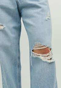 Vaqueros de mezclilla azul claro con detalles de rasgado en las rodillas. Presentan bordes deshilachados y un corte holgado, mostrando una tela texturizada con costuras visibles.