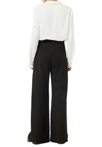 Blusa bianca a maniche lunghe con colletto, abbinata a pantaloni neri a gamba larga con vita alta, caratterizzati da una texture liscia e dettagli minimali.