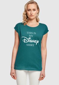 Mėlynos spalvos medvilninė marškinė su suktomis rankovėmis, priekyje yra balti užrašai "TAI YRA MANO Disney MARŠKINIAI" rašant neformaliu šriftu.