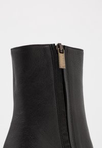 Black ankle boot with a textured leather finish, featuring a side zipper in a metallic tone and a smooth, structured upper.