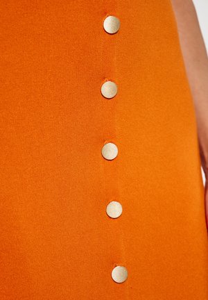 Oranžová látková sukně s vertikálním řádkem šesti kovových knoflíků. Textura je hladká, s mírným elastickým efektem a bez viditelných vzorů.