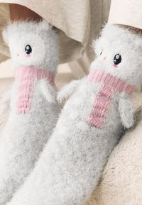 Calze grigie morbide che ricordano un pupazzo di neve, con polsino rosa a coste, dettagli del viso ricamati e piccoli bracci di tessuto su ciascun lato.