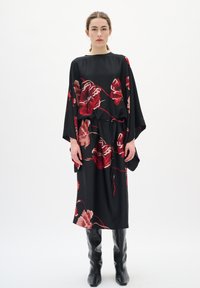Rochie neagră cu imprimeu floral vibrant în nuanțe de roșu și bej, croială lejeră, mâneci largi și talie legată, asortată cu cizme negre până la genunchi.