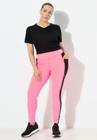 Svart t-shirt med kort ärm i kombination med högmidjade rosa leggings som har svarta sidopaneler och sömmar, avslutat med svarta träningsskor.