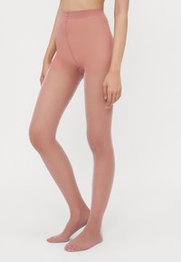 Gjennomsiktige, nude strømpebukser med høy midje. Glatt, glinsende overflate, tett passform gjennom hele benet. Mykt, lett materiale uten synlige mønstre.