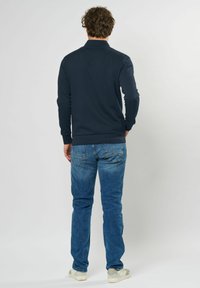 Marinblå långärmad pikétröja med krage, ihop med ljusblå jeans och vita sneakers. Tyget verkar slätt och avslappnat.