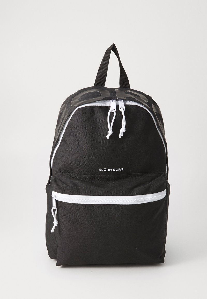 Mochila de tecido preta com um logotipo preto brilhante, detalhes em zíper branco e alças ajustáveis. Possui um bolso frontal com zíper e uma alça superior.