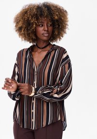 Striped button-up shirt in brown, cream, and navy, featuring a collar, long sleeves, and a relaxed fit with a curved hemline.