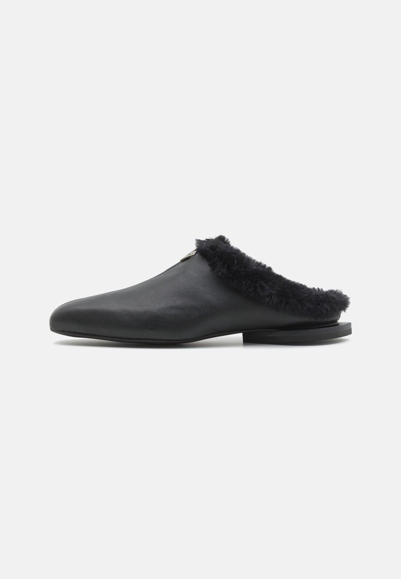 Chaussure slip-on en cuir noir avec un col en fourrure noire duveteuse, forme incurvée, semelle plate et design minimaliste.