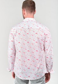Witte shirt met een roze flamingopatroon, lange mouwen, knoopsluiting en gebogen zoom. Stof is lichtgewicht en gestructureerd.