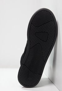 Černé tenisky s texturovanou gumovou podrážkou, která má vlnitý a tečkovaný vzor. Vyrobené z nubuku, s minimalistickým a elegantním designem.