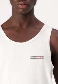 Top in cotone bianco con scollatura tonda e un piccolo logo "TOMMY JEANS" rosso e nero sul lato sinistro del petto.