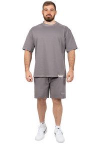 Grijze katoenen t-shirt met een relaxte pasvorm en korte mouwen, gecombineerd met bijpassende grijze shorts. Heeft een logo op zowel het shirt als de shorts.