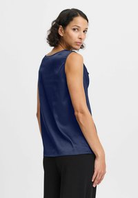 Top sin mangas de color azul marino, hecho de tela de satén, con un escote redondo y una textura suave, combinado con pantalones negros.