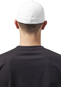 Hvid baseballkasket på en person set fra ryggen. Mørk t-shirt synlig under, der viser en glat stofstruktur.