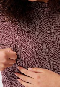 Burgunderfarbener Stoff mit Fischgrätenmuster; lange Ärmel und subtile Seitenreißverschlusdetails; glatte Textur und figurbetontes Design.