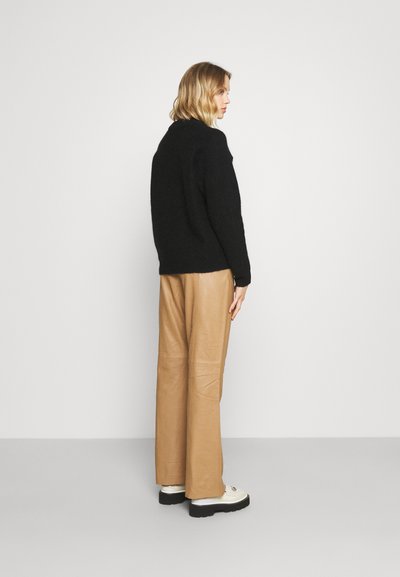 Pulover negru, pufos, din tricot, asociat cu pantaloni largi din piele bej. Look-ul este completat de pantofi albi cu talpă neagră.