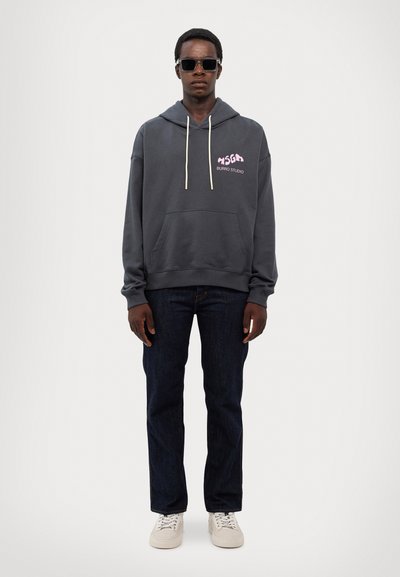 Mørkegrå hoodie med en frontlomme og cremefarvede snore, der har pink logo tekst. Kombineret med mørkeblå jeans og hvide sneakers.