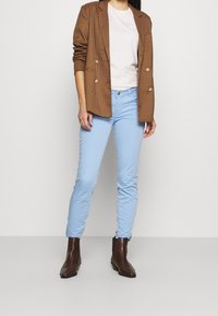Veste à carreaux marron portée sur un t-shirt rose clair, associée à un jean bleu clair slim et des bottines marron.