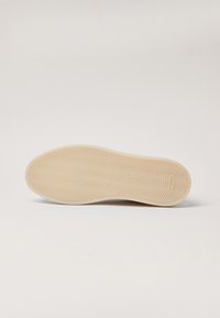 Suela de zapato de goma, color beige con un patrón de espiga texturizado, forma ligeramente curvada, bordes limpios y sin marcas ni detalles visibles.