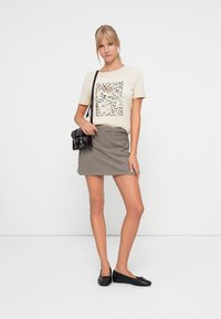 T-shirt beige a maniche corte con stampa leopardata metallica a quadrati, abbinato a una mini gonna grigia a quadretti e ballerine nere. Borsa a tracolla nera.