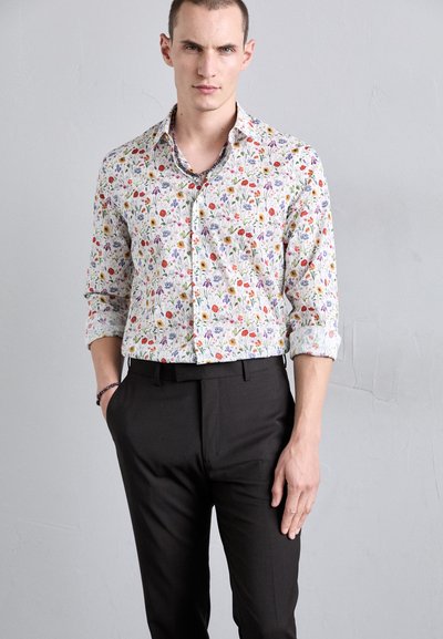 White button-up shirt with a colorful floral pattern, worn with black dress pants. Shirt features rolled sleeves and a slim fit design.
