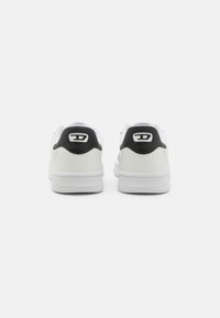 Vita idrottsskor i vitt med svarta hälaccenter, slät läderöverdel, rund tå och platt gummisula, med logotypdetalj på baksidan.