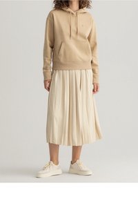 Béžová mikina s kapucí a přední kapsou, doplněná o plisovanou krémovou sukni a světle zbarvené tenisky. Pohodlný a ležérní outfit.