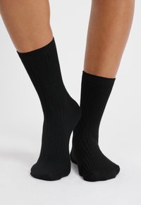 Calcetines negros de canalé fabricados en material suave, con una longitud hasta la mitad de la pantorrilla y un ajuste ceñido, con una textura suave y sin patrones visibles.