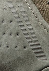 Matériau texturé gris avec un motif à points en relief et des accents en bandes diagonales. Présente une finition lisse et des détails cousus.