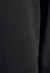 Schwarzer Stretchstoff mit einer glatten, gerippten Textur. Das Material wirkt weich und fällt eng, wobei es in bestimmten Bereichen einen subtilen Glanz zeigt.