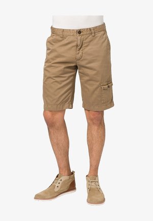 Shorts cargo en coton beige avec poche latérale, fermeture par bouton et ourlet retroussé. Portés avec des bottines claires.