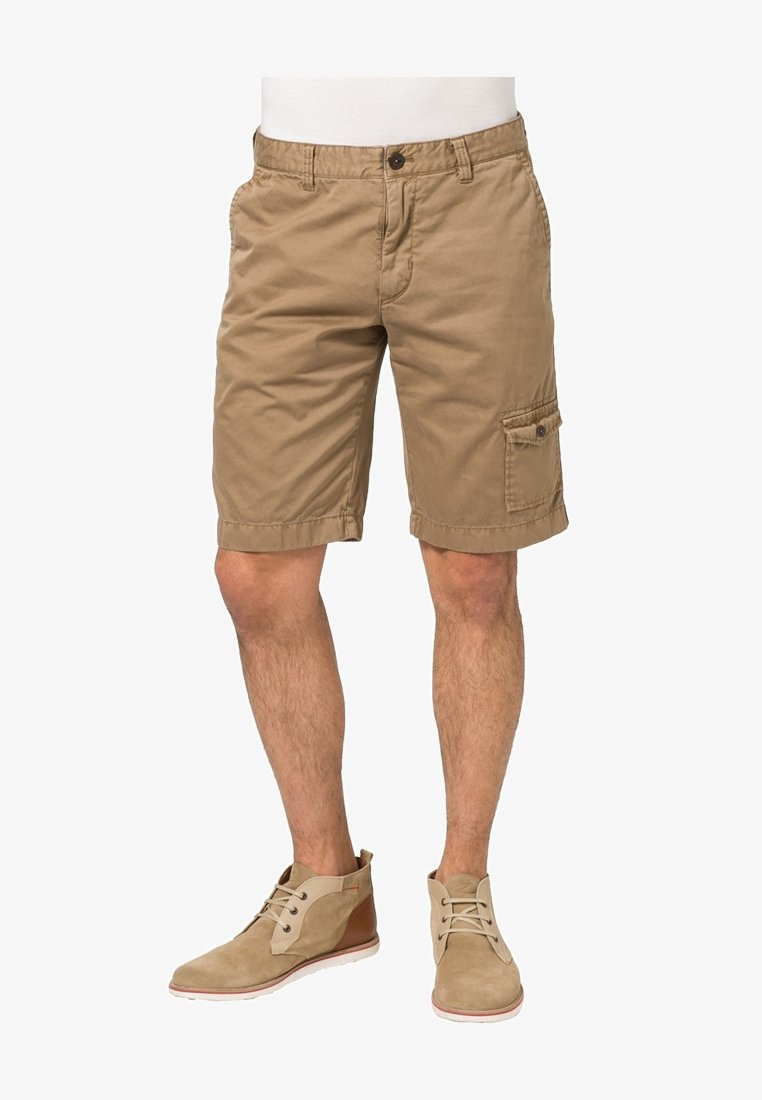 Shorts cargo en coton beige avec poche latérale, fermeture par bouton et ourlet retroussé. Portés avec des bottines claires.