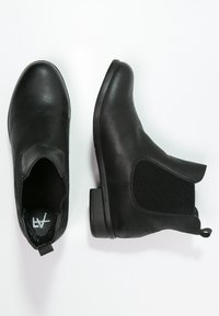 Stivali alla caviglia in pelle nera con pannelli elastici laterali, punte arrotondate, tacchi bassi e linguette per una facile calzata. Texture liscia con un design classico.