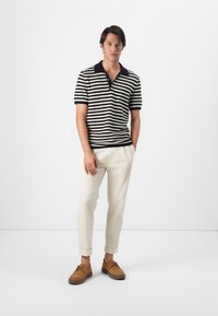 Camisa de polo a rayas en azul marino y crema, de manga corta, con cuello clásico; combinada con pantalones crema y zapatos de ante marrón con cordones.