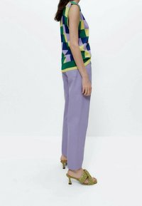 Top sin mangas de punto en un patrón geométrico verde, púrpura y amarillo; pantalones de talle alto en lavanda; sandalias de tacón trenzadas en verde.