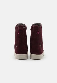 Paire de bottines en daim rouge foncé avec semelles beige, fermetures éclair latérales visibles et détail de couture rose sur les languettes à l'arrière.