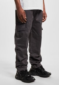 Pantalones cargo grises con múltiples bolsillos laterales, hechos de una tela duradera. Con un corte holgado y combinados con zapatillas negras.