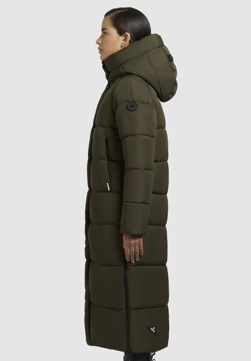 Langer, olivgrüner Puffer-Mantel mit Kapuze, ausgestattet mit einem gesteppten Design, einem Reißverschluss vorne und einem runden schwarzen Logo-Patch am Ärmel.