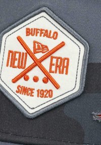 Gray fabric cap featuring a hexagonal patch. The patch displays "BUFFALO," "NEW ERA," and "SINCE 1920" in orange on a white background with crossed bats.