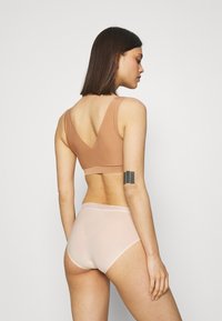 Soutien-gorge nu avec un design à dos en V ; tissu doux et extensible. Culottes roses taille haute avec une bordure en dentelle. Modèle vu de dos.
