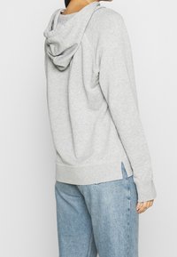 Szara hoodie z miękkiego materiału o luźnym kroju, z kapturem, bocznymi rozcięciami i prążkowanymi mankietami, w połączeniu z jasnoniebieskimi dżinsami.