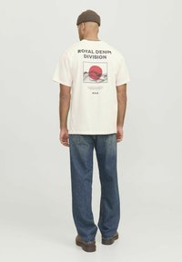 Cream oversized t-shirt featuring a graphic print with a red circle and line art on the back, paired with loose blue denim jeans.